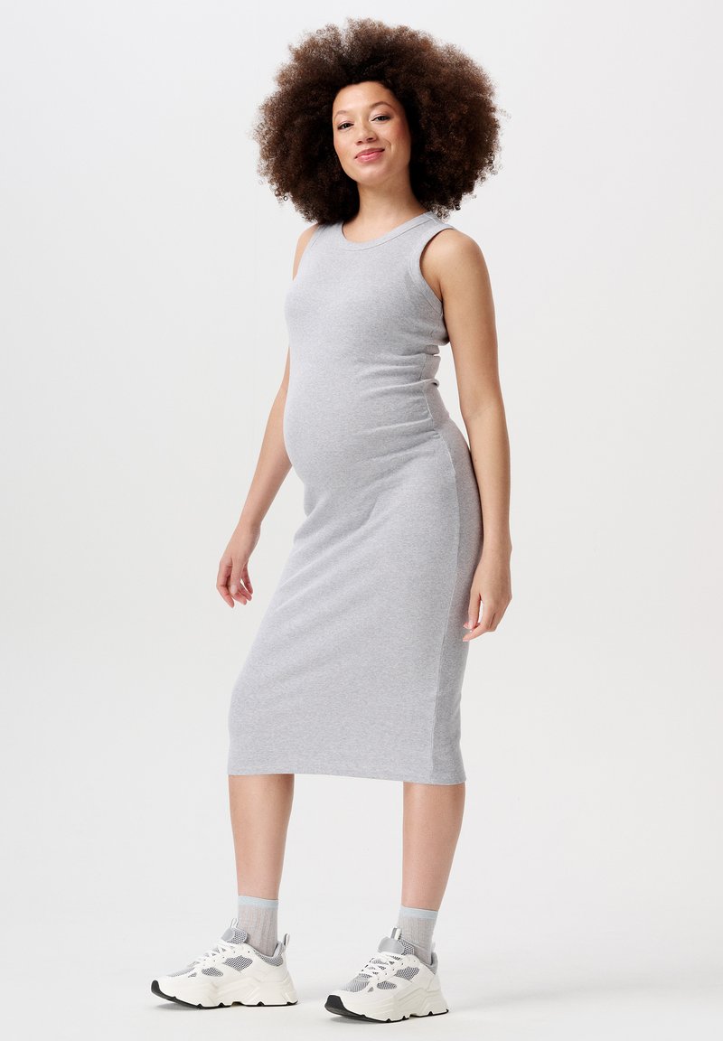 Robe de maternité grise côtelée avec une coupe ajustée, sans manches et longueur genou, assortie à des baskets blanches et grises.