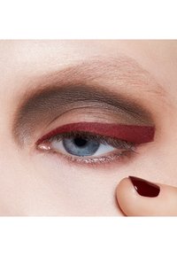 Nahaufnahme eines Auges mit brauem und rotem Lidschatten, glatter Textur und glänzendem Finish. Der Nagellack ist dunkelrot und betont den Look.