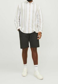 Biała koszula z guzikami, w pionowe beżowe paski, połączona z czarnymi szortami i białymi trampkami. Casualowy design, naturalna tekstura materiału.