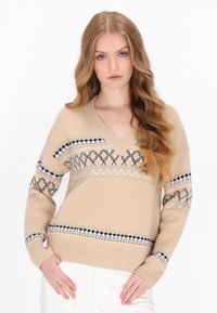 Beżowy sweter z dzianiny z dekoltem w serek, geometrycznym wzorem w odcieniach szarości i czerni na piersi i rękawach, z prążkowanymi mankietami i dołem.