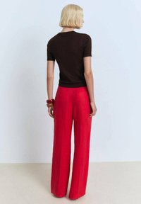 Haut marron à manches courtes associé à un pantalon rouge à larges jambes. Les pantalons ont une texture lisse, et le haut présente un design simple et ajusté.