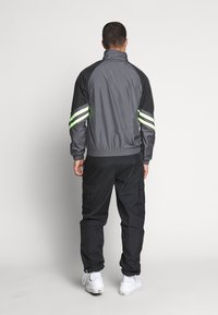 Gray athletic jacket with black sleeves and green stripes. Elastic waistband, zip collar, paired with black cargo pants and white shoes.