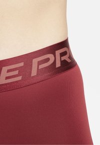 Bordowe legginsy z szerokim, textured pasem wytłaczanym z subtelnym logo "PRO". Tkanina ma gładką, elastyczną teksturę.