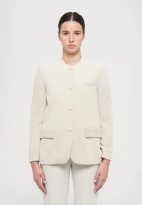 Giacca in corduroy beige chiaro con colletto rotondo, cinque bottoni e due tasche frontali. Tessuto testurizzato con una vestibilità su misura.
