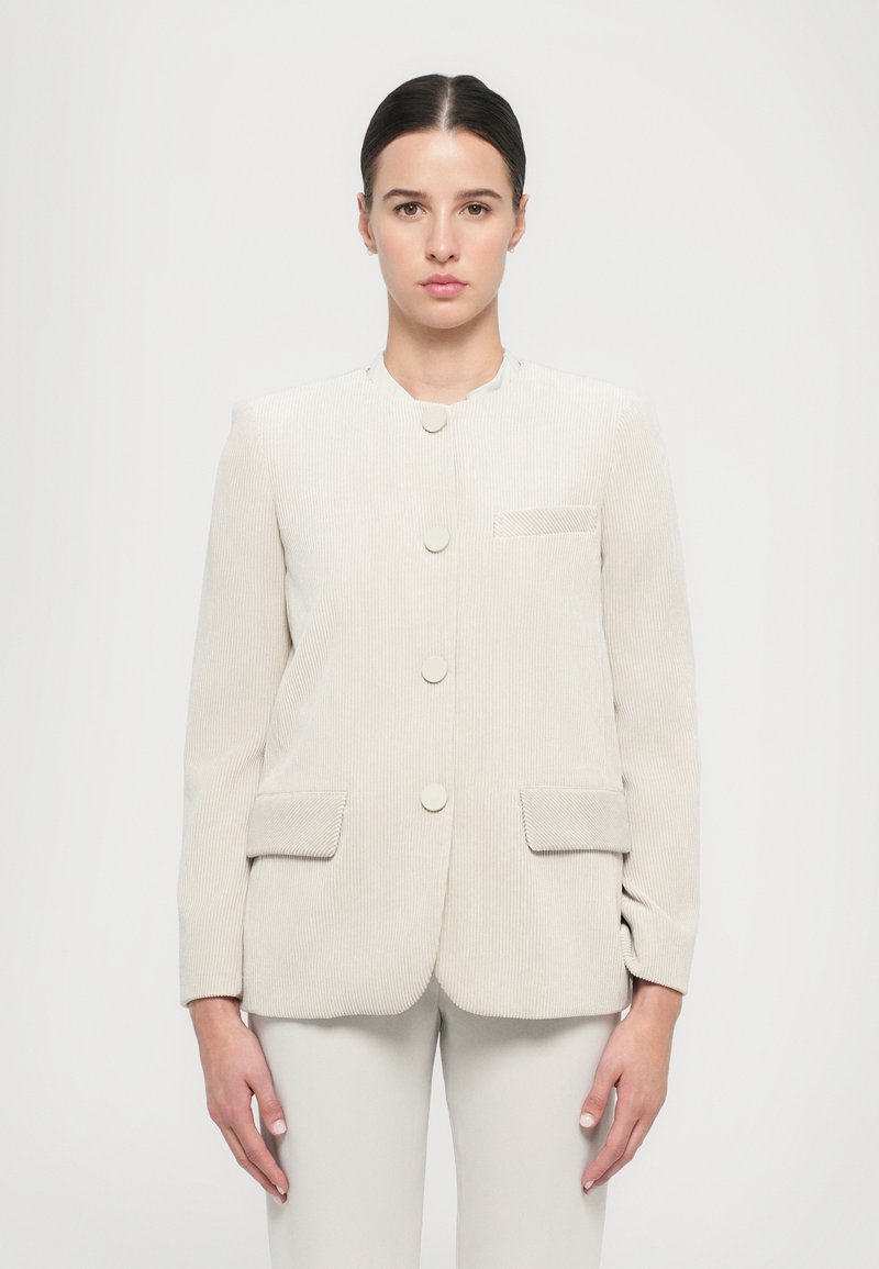 Giacca in corduroy beige chiaro con colletto rotondo, cinque bottoni e due tasche frontali. Tessuto testurizzato con una vestibilità su misura.