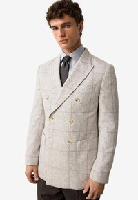 Dobbeltbrystet blazer i lys grå houndstooth-vævning, med guldknapper og en tekstureret stoffinish. Sættes sammen med en ternet skjorte.