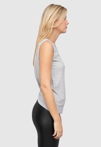 Lys grå ermeløs topp med et strukturert hullet mønster, tettsittende design og rund hals, kombinert med sorte leggings.
