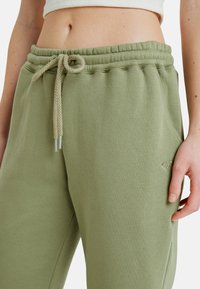 Lichtgroene joggingsbroek van zachte stof, met een elastische tailleband en een trekkoord, en zijzakken. Kleine logo-accent op de zak.