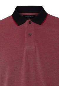 Rotes, strukturiertes Poloshirt mit schwarzem Kragen und roten Akzenten. Verfügt über drei Knöpfe und ein Etikett mit der Aufschrift "ANDREW JAMES REGULAR FIT."