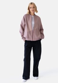 Jasnoróżowa bomberka na zamek z opadającymi ramionami, w połączeniu z luźnymi czarnymi spodniami. Biała koszulka pod spodem, noszona z białymi skarpetkami.