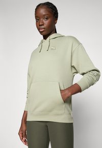 Felpa verde chiaro con tasca frontale, cappuccio con cordino e logo ricamato. Tessuto morbido e polsini a costine. Abbinata a leggings coordinati.