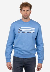 Sudadera azul claro con cuello redondo y mangas largas. Presenta un diseño gráfico con franjas horizontales y un logo en forma de 'A' en el pecho.