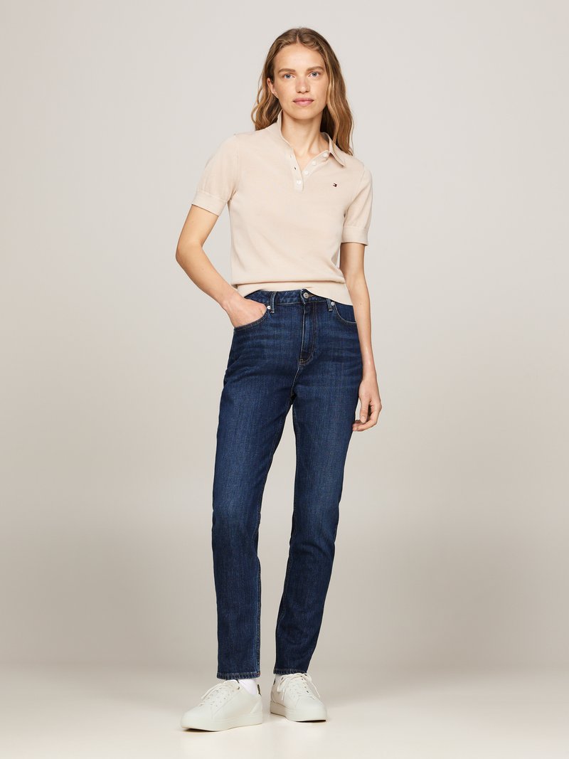 Beige polo skjorte med knappestolpe, kombinert med mørkeblå slim-fit jeans. Hvite sneakers fullfører antrekket. Enkelt og uformelt design.