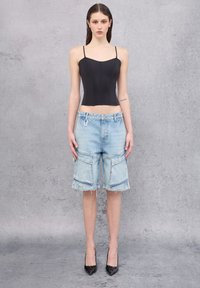 Zwarte korsettop met dunne straps, gecombineerd met lichtblauwe denim cargo shorts met patch pockets en rafelige zomen. Zwarte hoge hakken.