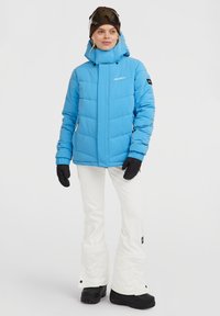 Blauwe geïsoleerde jas met ritszakken en een capuchon, gecombineerd met witte skibroek en zwarte handschoenen, ontworpen voor wintersport.
