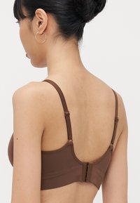 Reggiseno marrone con spalline regolabili, tessuto liscio e chiusura con gancio e asola sul retro. Design minimalista con un aspetto senza cuciture.