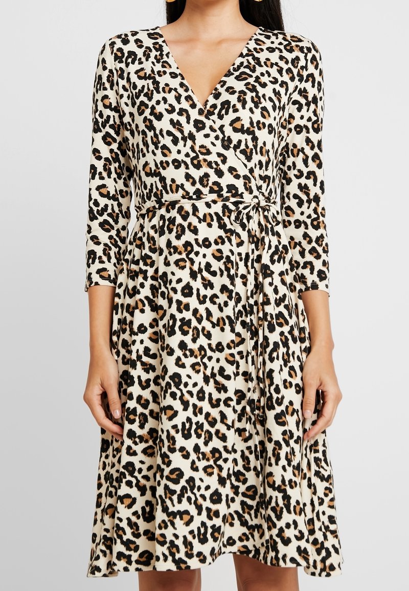 Sukienka typu wrap w lekkim materiale z kremowym tłem i czarnymi oraz brązowymi plamkami w leopardzie, z długimi rękawami i wiązanym detalem w talii.