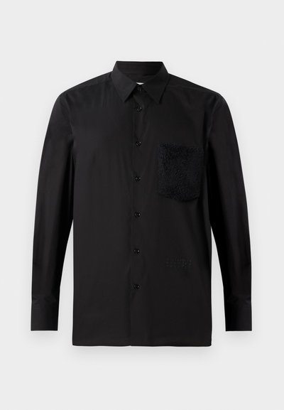 Camisa preta de manga longa com um bolso texturizado escuro, fecho de botão e detalhe subtil da marca perto da bainha. Tecido suave.