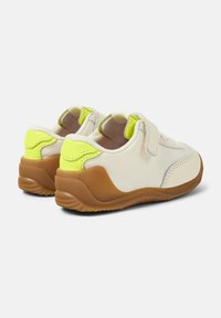 Le scarpe da ginnastica presentano una tomaia in tessuto crema con accenti verde neon, una suola in tan testurizzata e una cinghia in Velcro per una facile regolazione.