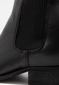 Bottine en cuir noir avec des panneaux latéraux en élastiquefroid côtelé et un petit talon en bois. Texture lisse avec des détails de couture contrastants.