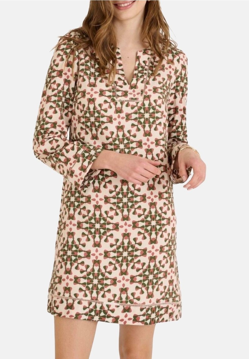 Femme portant une robe à manches longues, longueur genou, avec un motif floral géométrique rose, vert et marron.