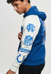 Blue and white hoodie featuring a large NFL logo, graphic prints on the back, and text accents on sleeves. Soft fabric, relaxed fit.