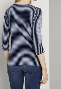 Navy blue and white striped shirt with three-quarter sleeves, round neckline, and a fitted design. Made of soft, smooth fabric.