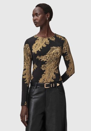 Langarmtop van zwart stof versierd met ingewikkelde gouden barokpatronen. Gecombineerd met hoge, zwarte leren broek.