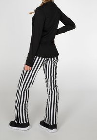 Svart långärmad topp i kombination med vit och svart vertikalt randiga byxor. Byxorna har en tight passform och en lätt utsvängning vid ankeln. Svarta sneakers.