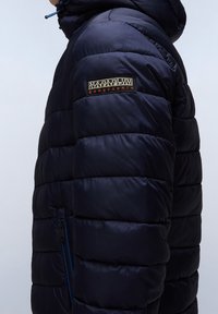 Granatowa kurtka puchowa o pikowanym wzorze, z zamykanym na zamek kieszeniem i naszywką z logo na górnej części rękawa. Miękki, lekki materiał.