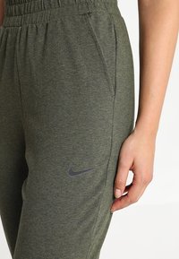 Zelené sportovní tepláky s texturovaným povrchem, mají elastický pas, boční kapsy a decentní šedé logo Nike na levé straně.