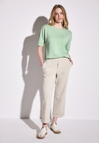 Haut vert à manches courtes associé à un pantalon beige coupé, tous deux en tissu doux. Les chaussures sont crème avec des accents marron, offrant un look décontracté.