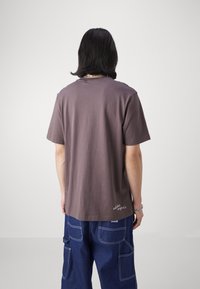 Kortärmad mauve t-shirt i bomull. Har en rund halsringning och en liten logodetail vid fållen. Bärs med lösa blå cargobyxor.