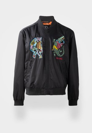 Chaqueta bomber negra con puños acanalados, que presenta coloridos diseños bordados de un personaje y un cocodrilo en la parte delantera. Cierre con cremallera.