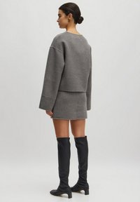 Grauer verkürzter Pullover mit überschnittenen Schultern, kombiniert mit einem passenden grauen Minirock. Schwarze kniehohe Stiefel mit niedrigem Absatz runden den Look ab.