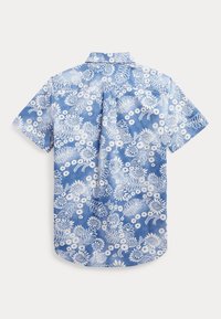 Camicia a maniche corte in tessuto azzurro chiaro con motivo floreale bianco, colletto a camicia e orlo curvo. Presente un effetto tie-dye sottile.