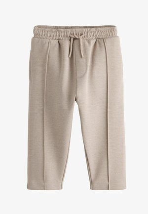 Beige elastiske bukser med synlige sømme foran og bundet snøre, lavet af tekstureret stof, vist på hvid baggrund.