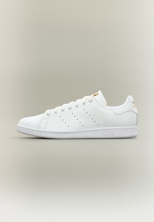 Witte leren Adidas Stan Smith sneaker met geperforeerde strepen, gouden logodetails op de tong en hiel en witte rubberen zool, zijaanzicht.
