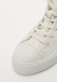 Baskets en cuir blanc avec une surface texturée, bout rond et lacets plats. Comprend une semelle en caoutchouc blanc avec une semelle à motif antidérapant.