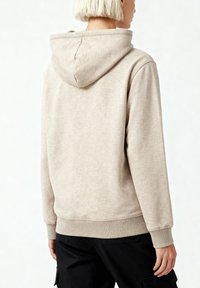 Sweat à capuche beige avec un cordon de serrage, des poignets et un ourlet côtelés. Le tissu semble doux, avec une finition texturée. La vue de dos montre la coupe décontractée.