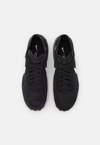 Scarpe sportive nere con una tomaia in tessuto texturizzato, lacci piatti, logo Nike bianco sul lato e una suola bianca imbottita.