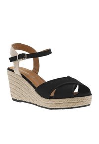 Black wedge sandal with a textured espadrille sole, featuring a woven ankle strap and crisscross design on the front.