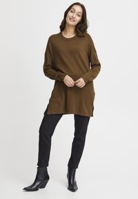 Tunic lung cu mânecă lungă de culoare maronie, cu slituri laterale, realizat dintr-un material moale. Asortat cu pantaloni negri slim-fit și cizme negre până la gleznă.