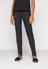 Sorte treningsbukser med et teksturert bladmønster, med en slim fit og elastisk midjebånd, akkompagnert av gule logodetaljer.