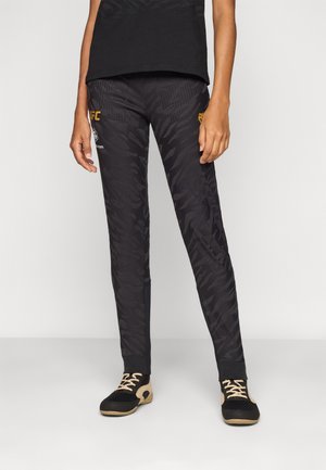 Sorte treningsbukser med et teksturert bladmønster, med en slim fit og elastisk midjebånd, akkompagnert av gule logodetaljer.