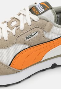 Adidași Puma cu un tors negru din suede și plasă bej, accente din piele portocalie, șireturi albe și o talpă din cauciuc negru.