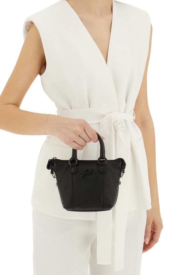 Borsa a mano in pelle nera con finitura a pietra, manici arrotondati, hardware argentato e logo incastonato; abbinata a una camicia bianca con cintura.