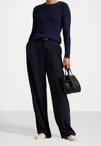 Osoba v námořnickém svetr s pleteným vzorem, širokých námořnických kalhotách, bílých teniskách, jednoho drží černou koženou kabelku.