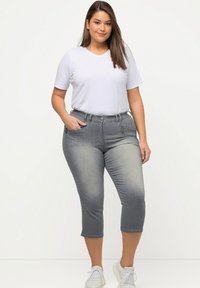 Capri en denim gris avec un design ajusté, doté d'une taille mi-haute, de poches avant et d'une texture légèrement décolorée. Associé à un T-shirt blanc.
