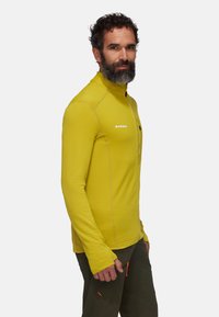 Maglietta sportiva a maniche lunghe di un brillante giallo, con colletto a mezza zip, texture a coste e cuciture a contrasto. Logo posizionato sul petto.
